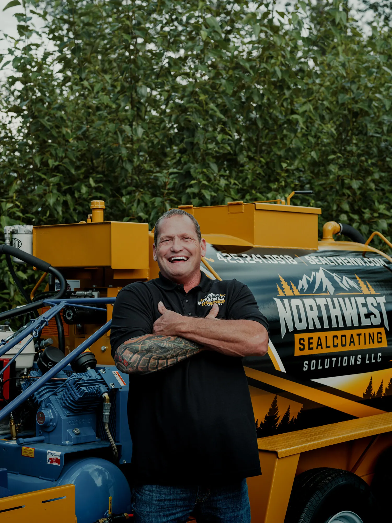 Chad Moudy, owner of Northwest Sealcoating Solutions, laughing next to the company trailer.