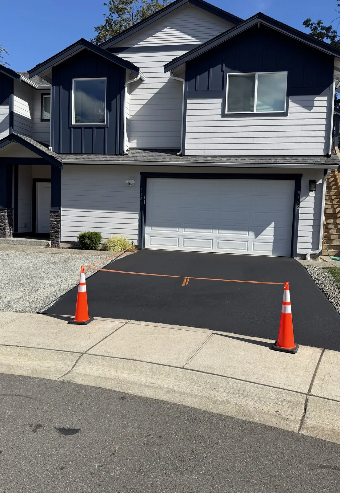 The same driveway after sealcoating by Northwest Sealcoating Solutions: freshly sealed, jet-black asphalt with cones and safety tape still in place.