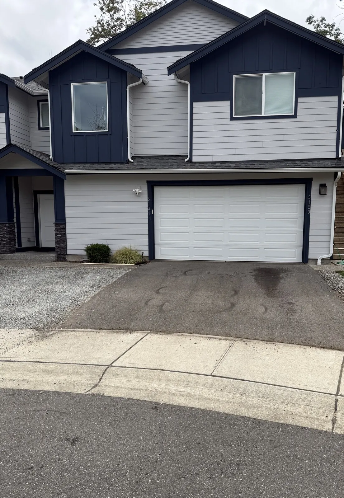 A SeaTac driveway before sealcoating: faded, oil-stained asphalt in front of a two-story home.