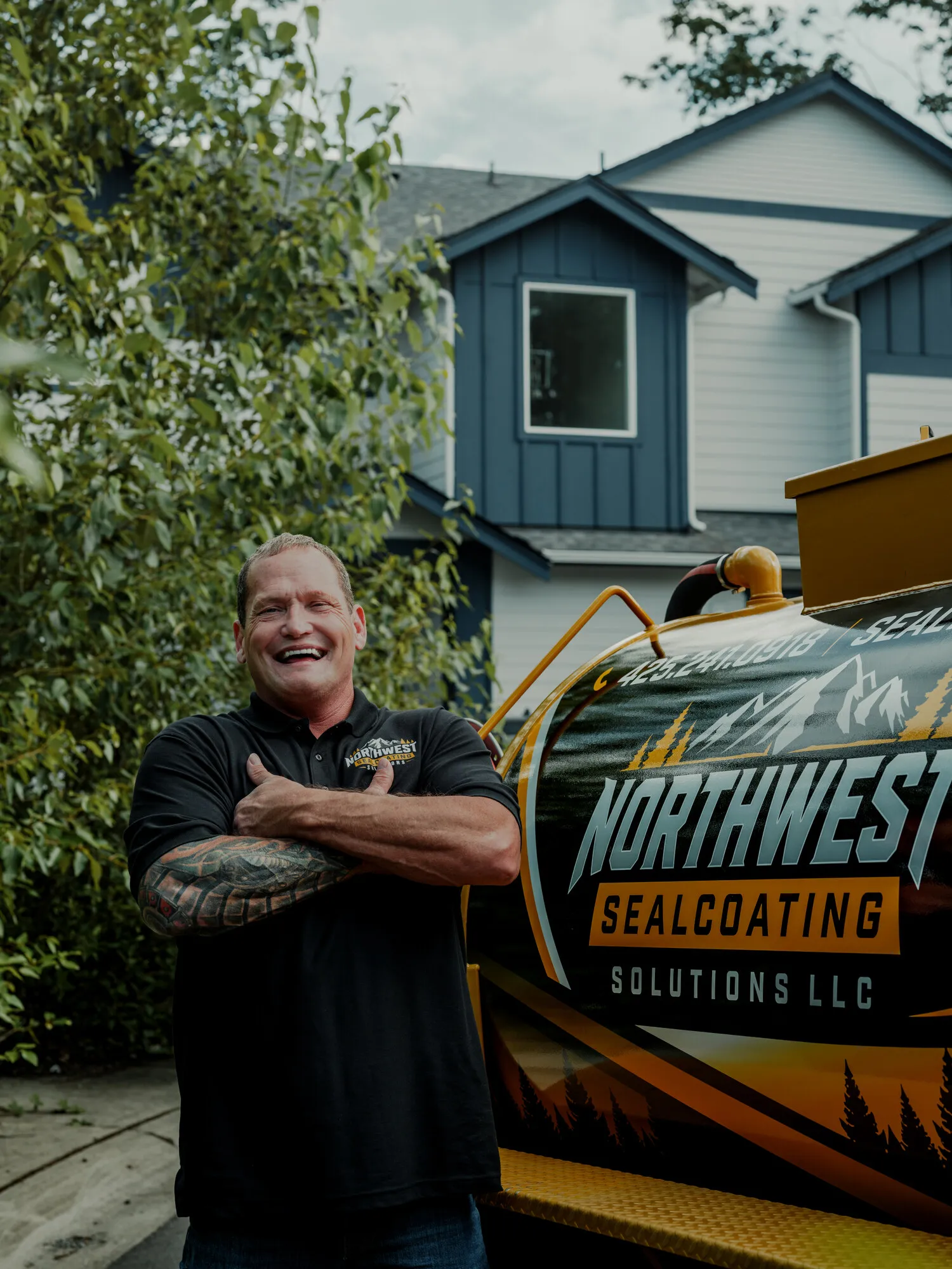 Chad, owner of Northwest Sealcoating Solutions, smiling in front of his branded sealcoating trailer.