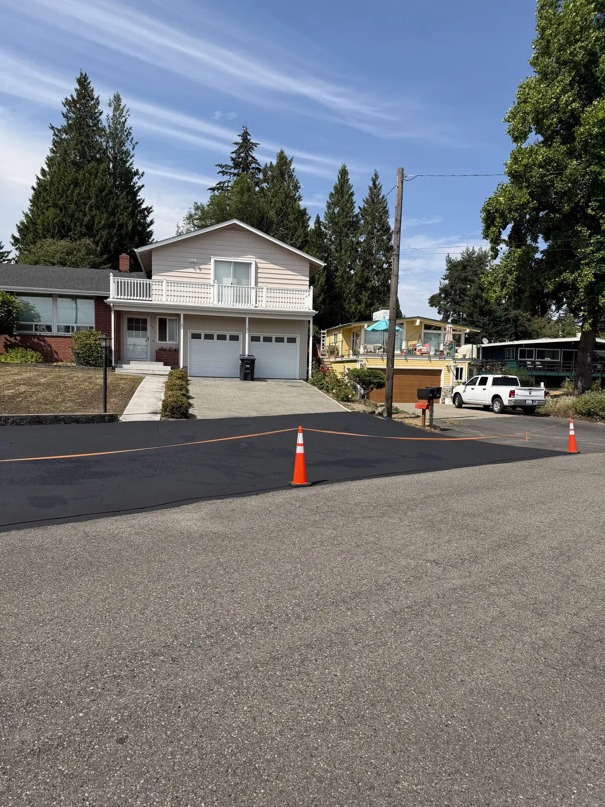 The finished shared driveway, sealed deep black, with cones and safety tape in place.