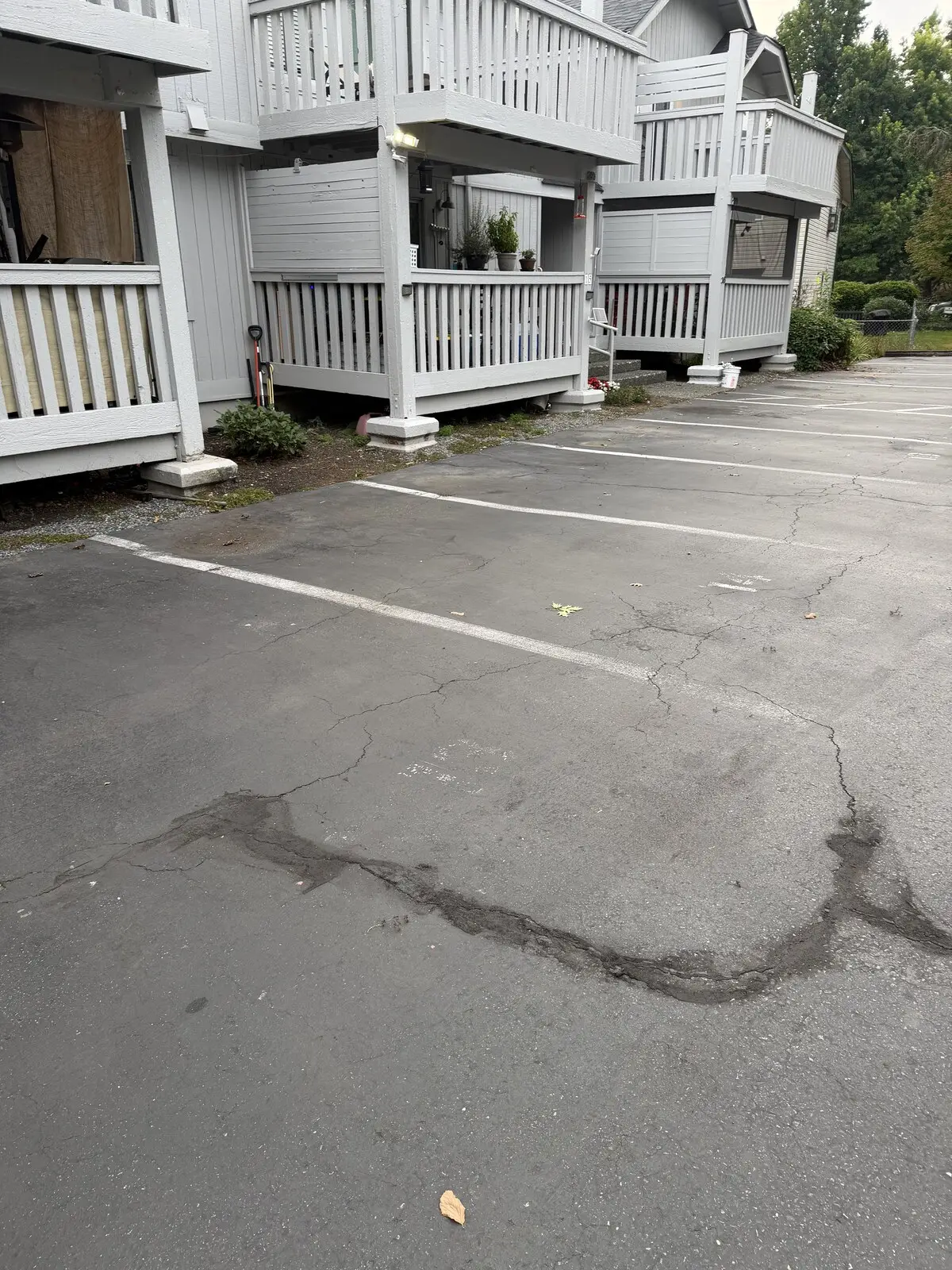 The apartment lot before sealcoating: gray, oxidized asphalt with a broken-up cracked patch spreading across the stalls.