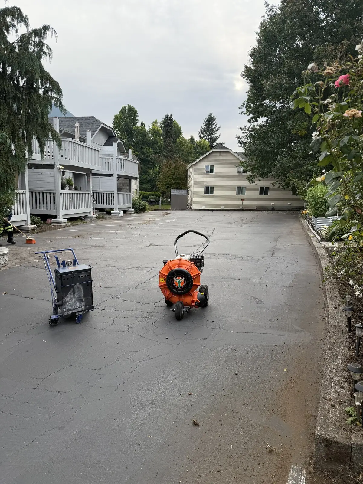 The lot washed down and the blower staged, still unsealed, with water standing on the gray asphalt.