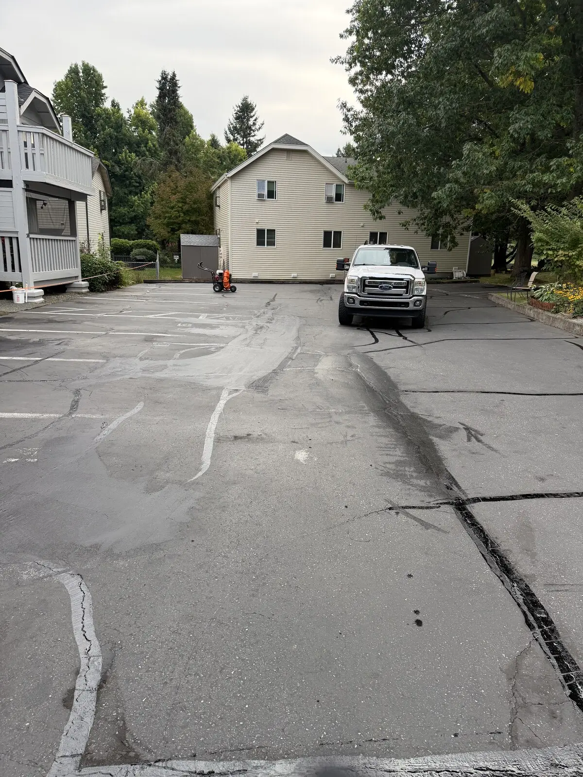 The apartment lot before sealcoating: oxidized gray asphalt with long cracks running across the drive lane.