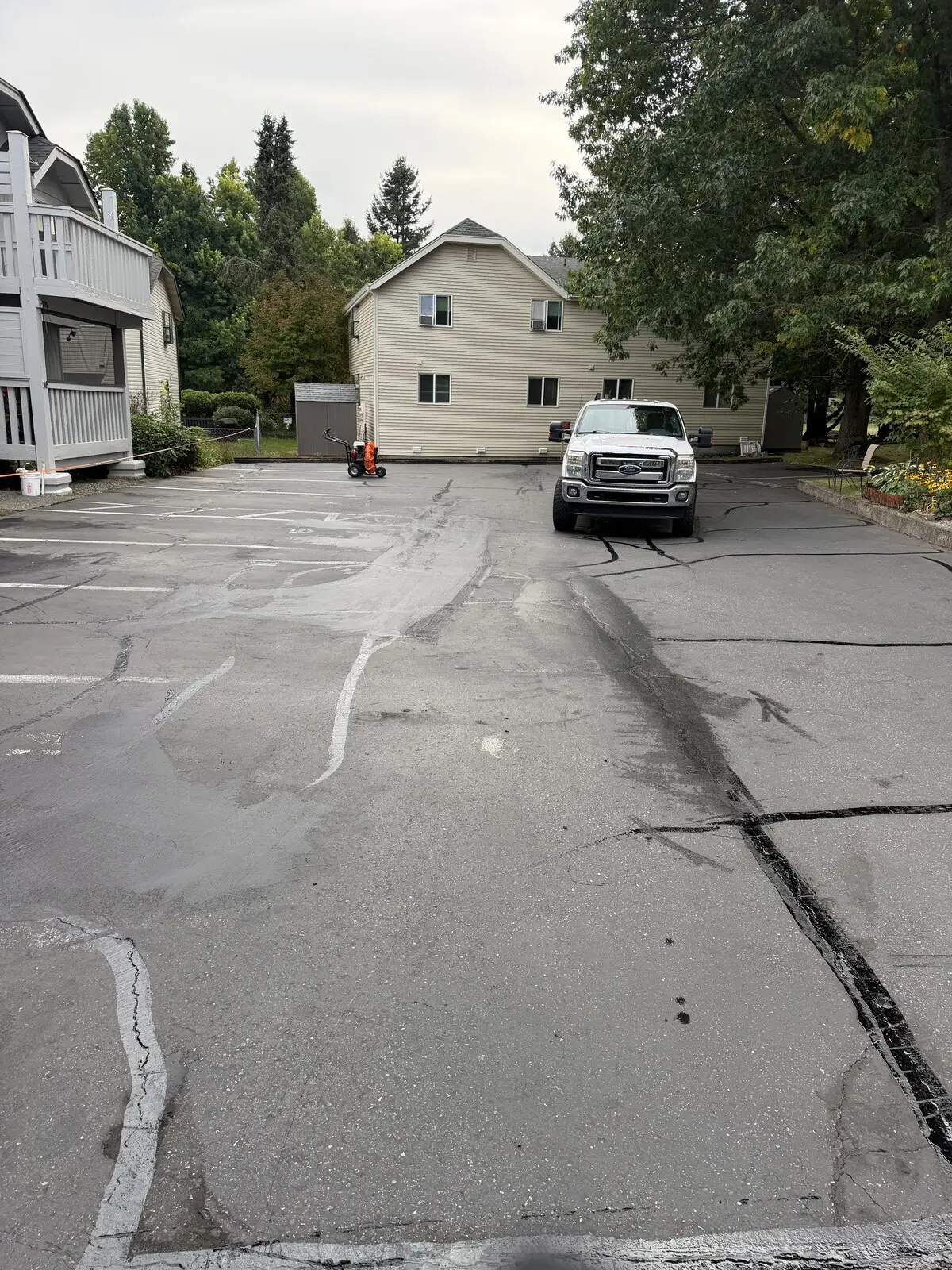A wide view of the lot before sealing, long cracks running down the drive lane toward the buildings.
