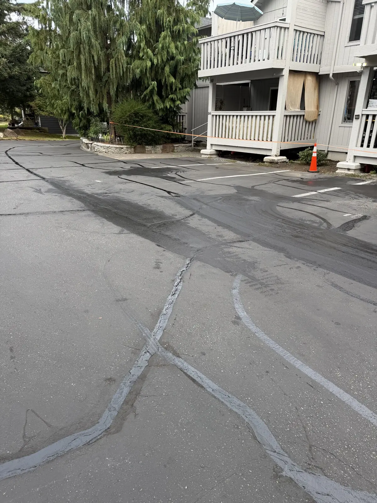 Crack fill laid into the splits across the lot, with a cone and safety tape holding the area off.