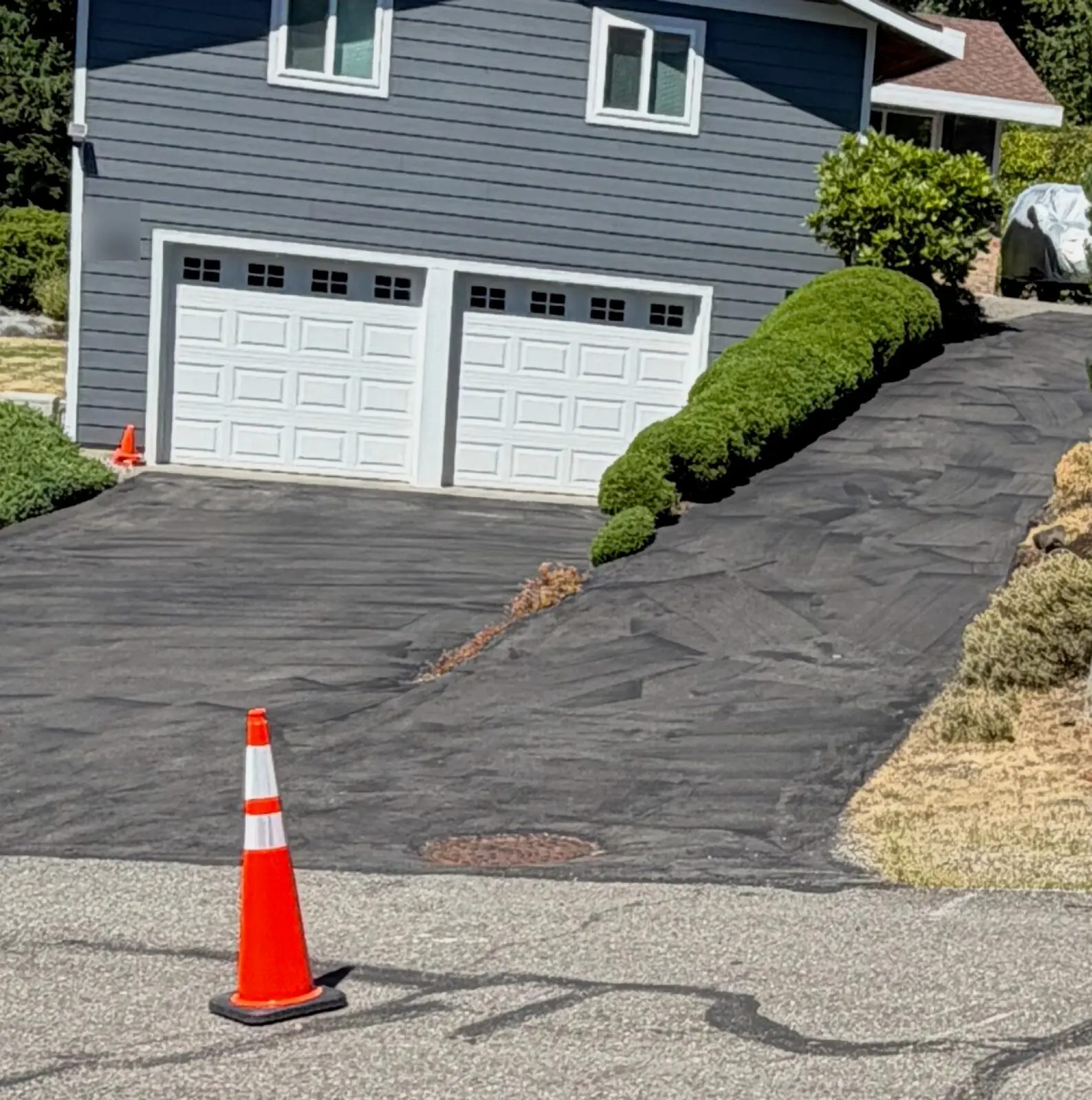 A steep Seattle driveway before sealcoating: patchy, washed-out gray asphalt with debris on the surface.